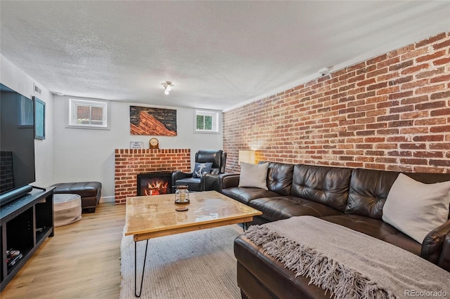 living area featuring wood finished floors, a fireplace, brick wall, a textured ceiling, and baseboards