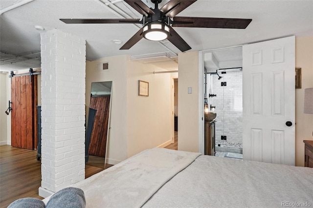 bedroom with wood finished floors, a barn door, baseboards, ensuite bath, and a ceiling fan