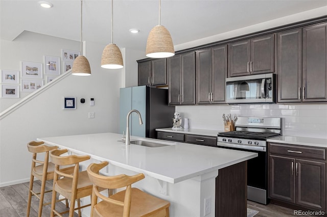 kitchen with hardwood / wood-style floors, an island with sink, appliances with stainless steel finishes, a breakfast bar, and sink