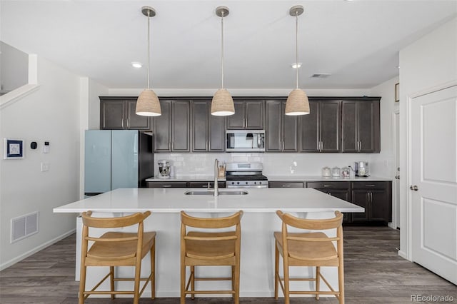 kitchen featuring dark brown cabinets, hanging light fixtures, an island with sink, appliances with stainless steel finishes, and dark hardwood / wood-style floors