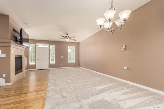 unfurnished living room with ceiling fan with notable chandelier, lofted ceiling, a tiled fireplace, and light hardwood / wood-style floors