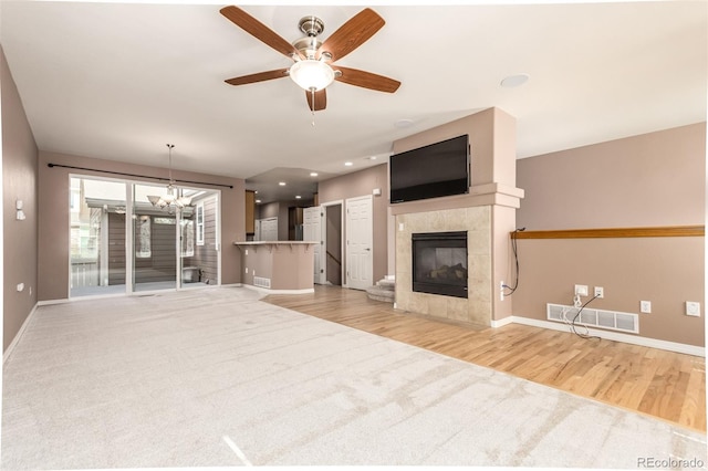 unfurnished living room with ceiling fan, a tiled fireplace, and light hardwood / wood-style floors