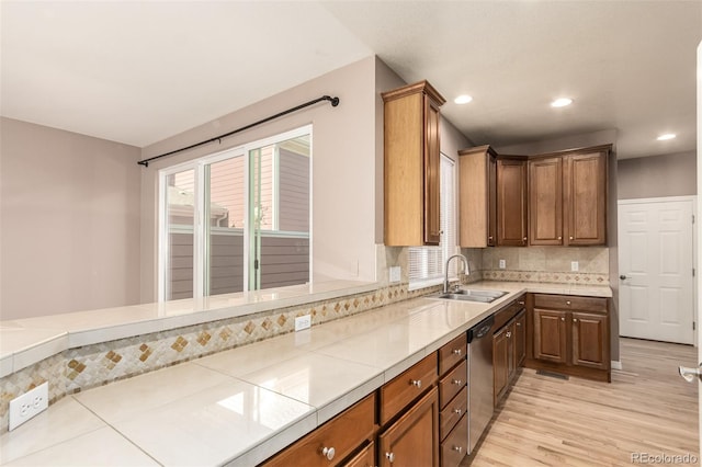 kitchen with light wood-type flooring, decorative backsplash, stainless steel dishwasher, sink, and tile countertops