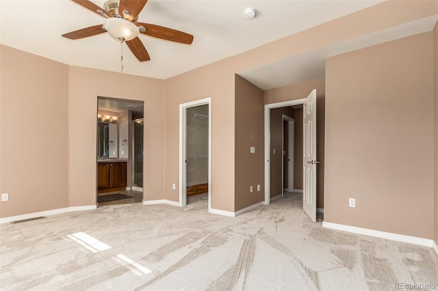 unfurnished bedroom featuring a spacious closet, ceiling fan, a closet, ensuite bathroom, and light colored carpet