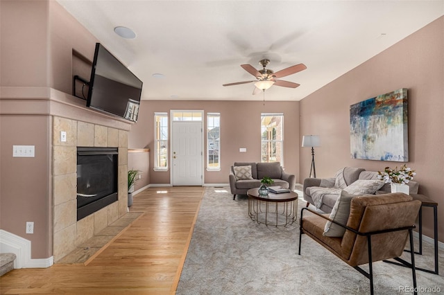 living area featuring light wood-style floors, ceiling fan, a fireplace, and baseboards