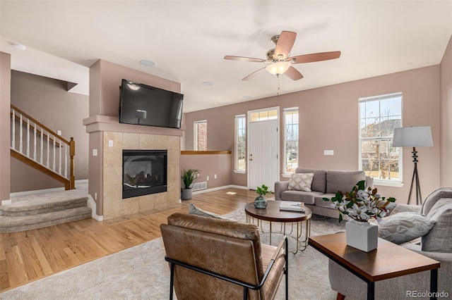 living area featuring a fireplace, visible vents, wood finished floors, baseboards, and stairs