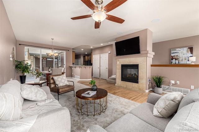 living room featuring a tile fireplace, light wood-style flooring, ceiling fan with notable chandelier, visible vents, and baseboards