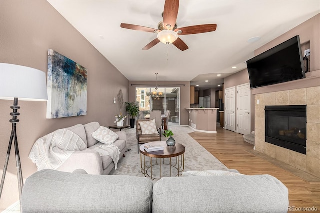 living room featuring recessed lighting, ceiling fan with notable chandelier, a fireplace, baseboards, and light wood finished floors