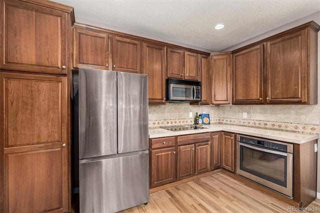 kitchen with brown cabinets, stainless steel appliances, light countertops, backsplash, and light wood-type flooring