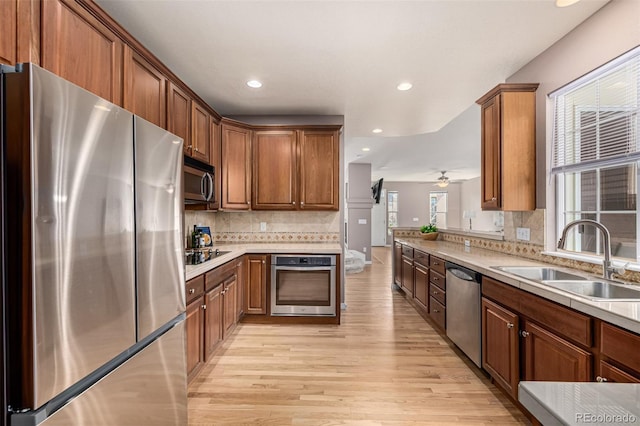 kitchen featuring light wood finished floors, light countertops, backsplash, appliances with stainless steel finishes, and a sink