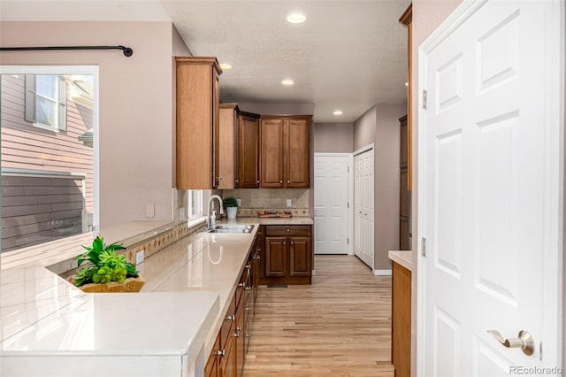 kitchen with recessed lighting, a sink, light countertops, light wood finished floors, and tasteful backsplash