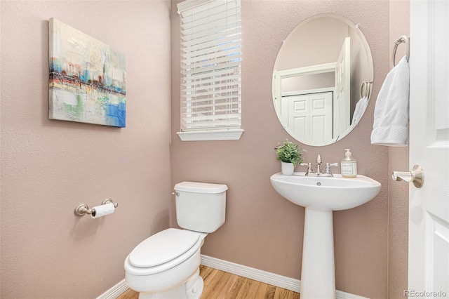 half bath featuring baseboards, a sink, toilet, and wood finished floors