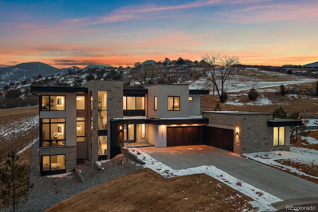 view of front of home featuring driveway, stone siding, an attached garage, a mountain view, and stucco siding