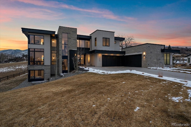 contemporary house featuring stone siding, a lawn, and driveway