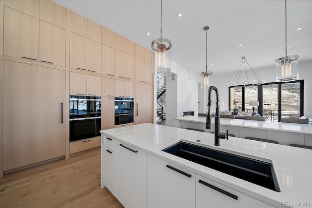 kitchen with light wood-style flooring, modern cabinets, hanging light fixtures, light countertops, and a sink