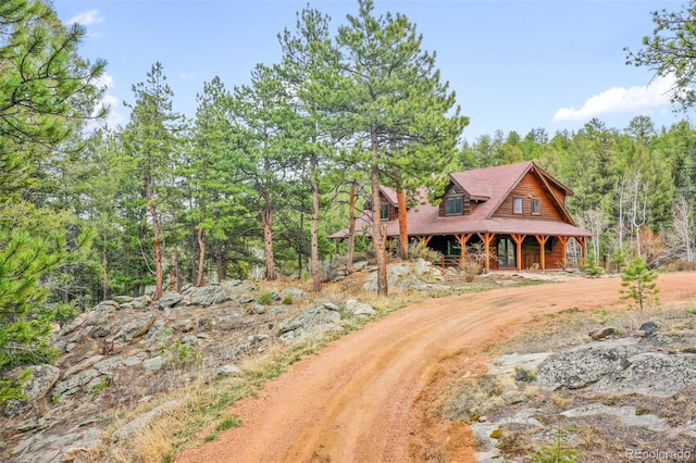 cabin featuring a view of trees, covered porch, and driveway