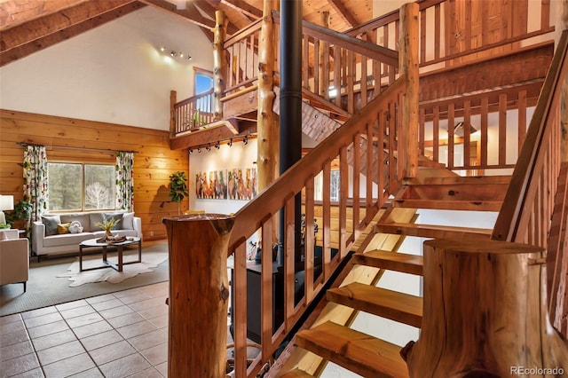stairs with tile patterned flooring, beam ceiling, wooden walls, and high vaulted ceiling