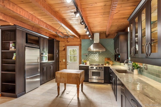 kitchen featuring wall chimney range hood, rail lighting, a sink, light stone counters, and premium appliances