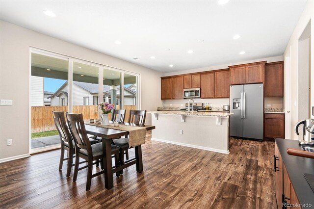 18077 E 99th Ave, Commerce City, CO 80022 - kitchen with stainless steel appliances, dark wood-type flooring, a center island with sink, a kitchen breakfast bar, and baseboards