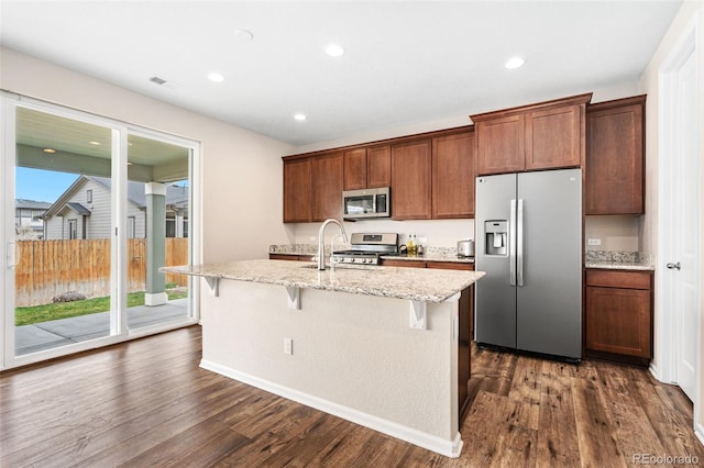 18077 E 99th Ave, Commerce City, CO 80022 - kitchen with appliances with stainless steel finishes, a kitchen island with sink, dark wood finished floors, a breakfast bar, and light stone countertops