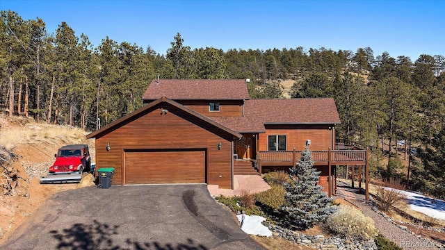 rustic home with an attached garage, aphalt driveway, a wooded view, and a wooden deck