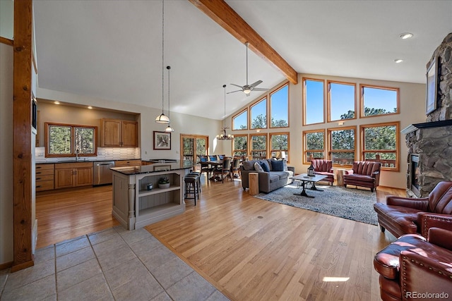 living room featuring light wood finished floors, high vaulted ceiling, beamed ceiling, and a stone fireplace