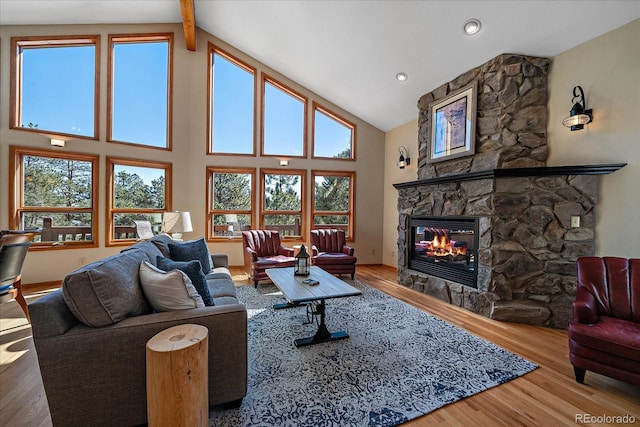 living area featuring high vaulted ceiling, a stone fireplace, wood finished floors, and a wealth of natural light