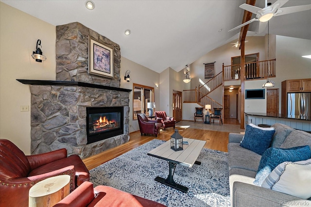 living room featuring a fireplace, a ceiling fan, wood finished floors, high vaulted ceiling, and stairs