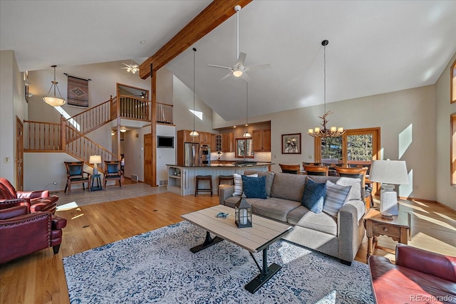 living area featuring stairs, beam ceiling, high vaulted ceiling, light wood-type flooring, and ceiling fan with notable chandelier