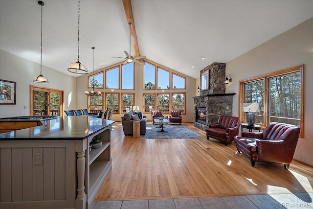 living area featuring beam ceiling, light wood finished floors, a stone fireplace, high vaulted ceiling, and baseboards