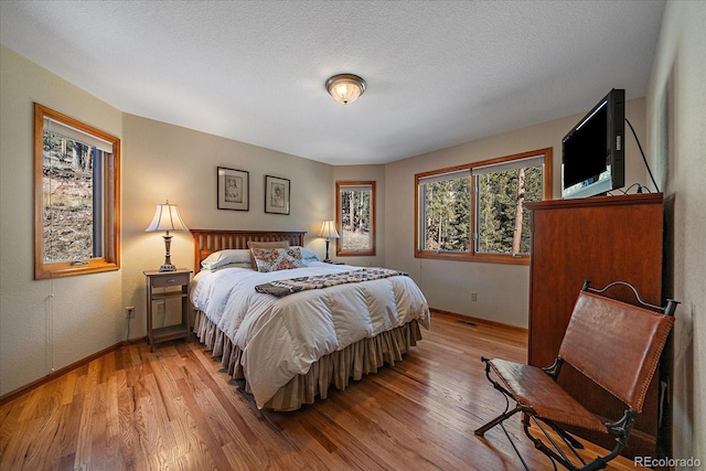 bedroom with light wood-type flooring, baseboards, and a textured ceiling