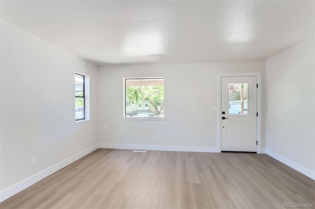 unfurnished room featuring a textured ceiling, a wealth of natural light, and light hardwood / wood-style flooring