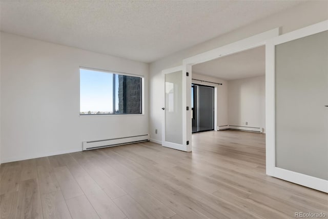 spare room featuring baseboard heating, a textured ceiling, and light wood-type flooring