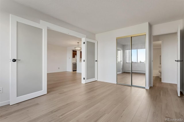 unfurnished bedroom featuring baseboard heating, light hardwood / wood-style floors, a textured ceiling, and a closet