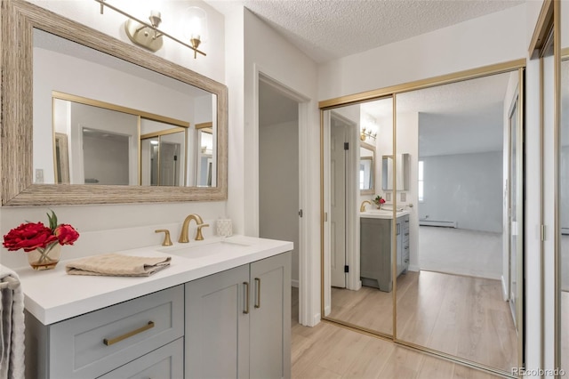 bathroom featuring vanity, a baseboard heating unit, a textured ceiling, and wood-type flooring