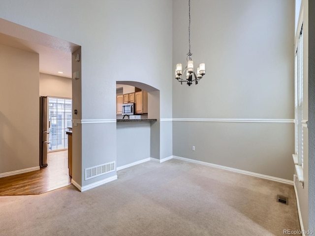 5155 W Quincy Ave Unit J103, Denver, CO 80236 - spare room featuring light carpet, a chandelier, arched walkways, and a high ceiling