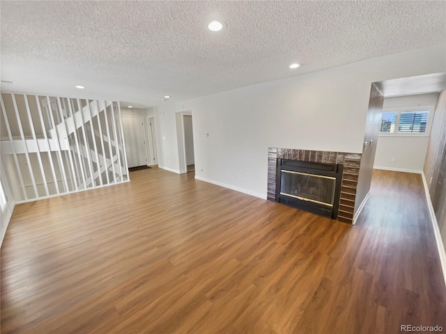 unfurnished living room with a textured ceiling, a brick fireplace, and hardwood / wood-style floors