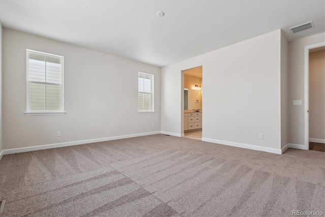 unfurnished bedroom with light carpet, ensuite bath, and multiple windows