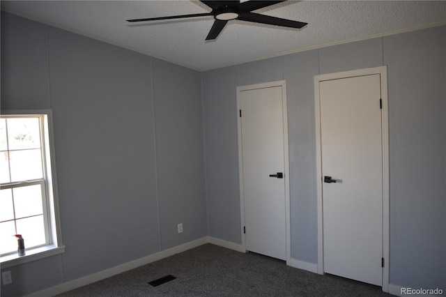 unfurnished bedroom with visible vents, ceiling fan, dark carpet, and a textured ceiling