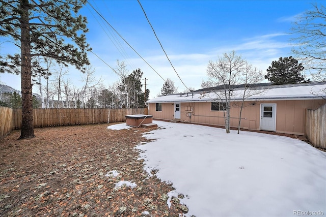 snow covered back of property with a hot tub