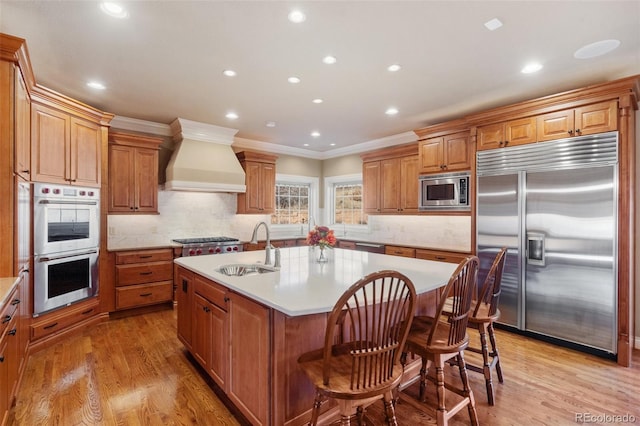 kitchen featuring sink, built in appliances, an island with sink, light hardwood / wood-style floors, and custom exhaust hood