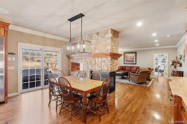 dining area with crown molding, light wood-type flooring, a fireplace, and a chandelier