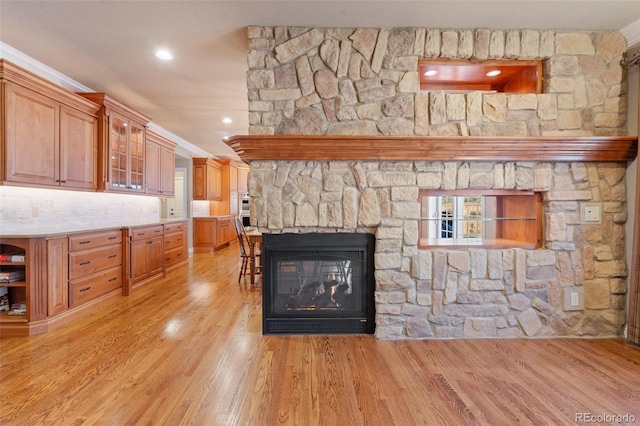 living room featuring a stone fireplace, ornamental molding, and light hardwood / wood-style flooring