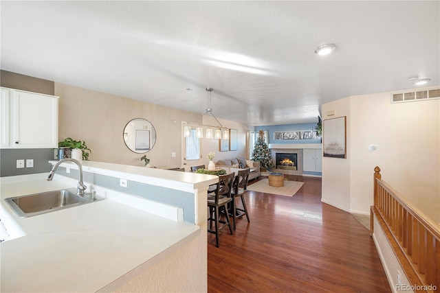 kitchen with sink, decorative light fixtures, a fireplace, dark hardwood / wood-style floors, and white cabinetry