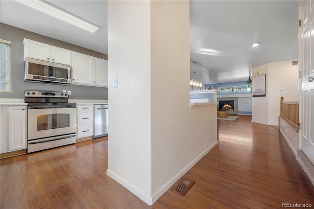 kitchen featuring a tile fireplace, white cabinetry, light wood-type flooring, and appliances with stainless steel finishes