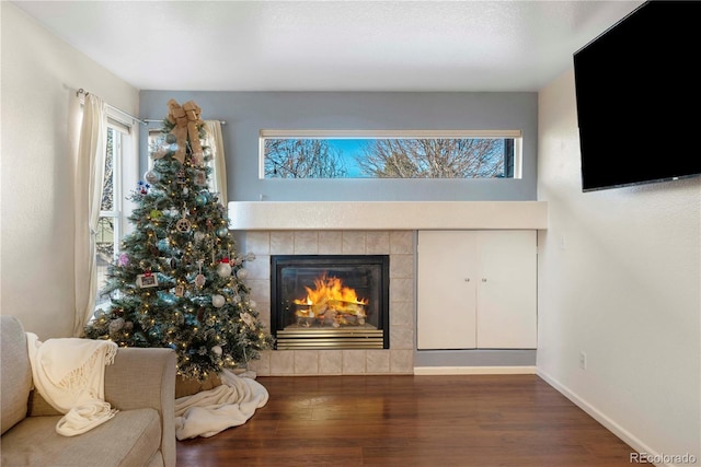 living room with a healthy amount of sunlight, dark wood-type flooring, and a tiled fireplace