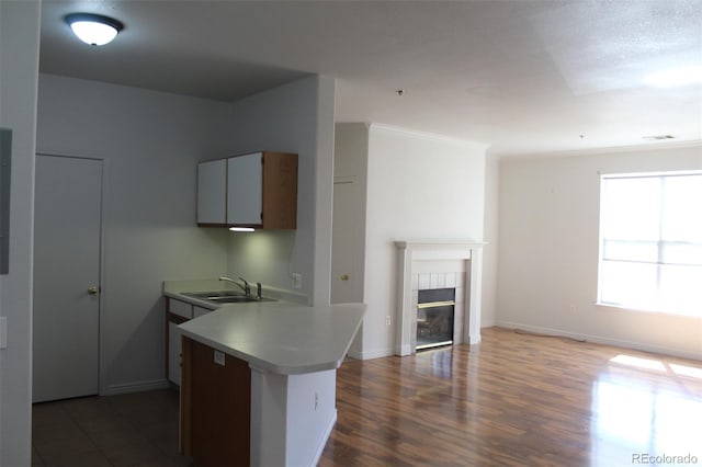 kitchen featuring dark wood-type flooring, kitchen peninsula, a tile fireplace, sink, and crown molding