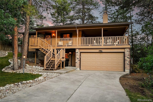 view of front of home featuring a porch, concrete driveway, stairs, an attached garage, and a chimney