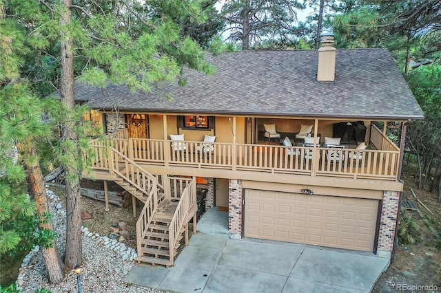 view of front of house featuring roof with shingles, a chimney, an attached garage, driveway, and covered porch