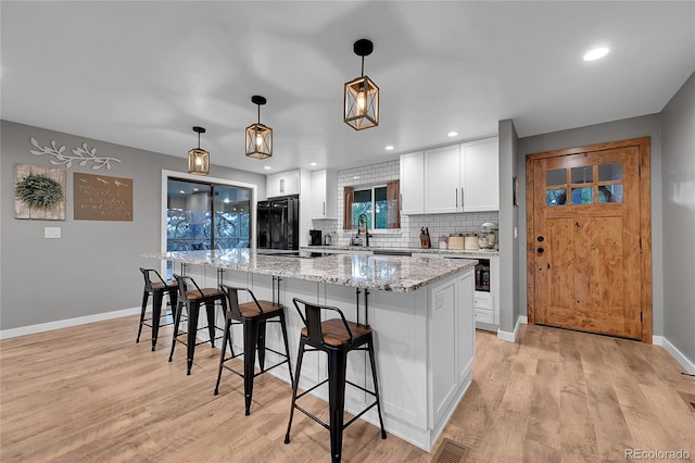 kitchen featuring black refrigerator, a kitchen breakfast bar, light wood-style floors, backsplash, and recessed lighting